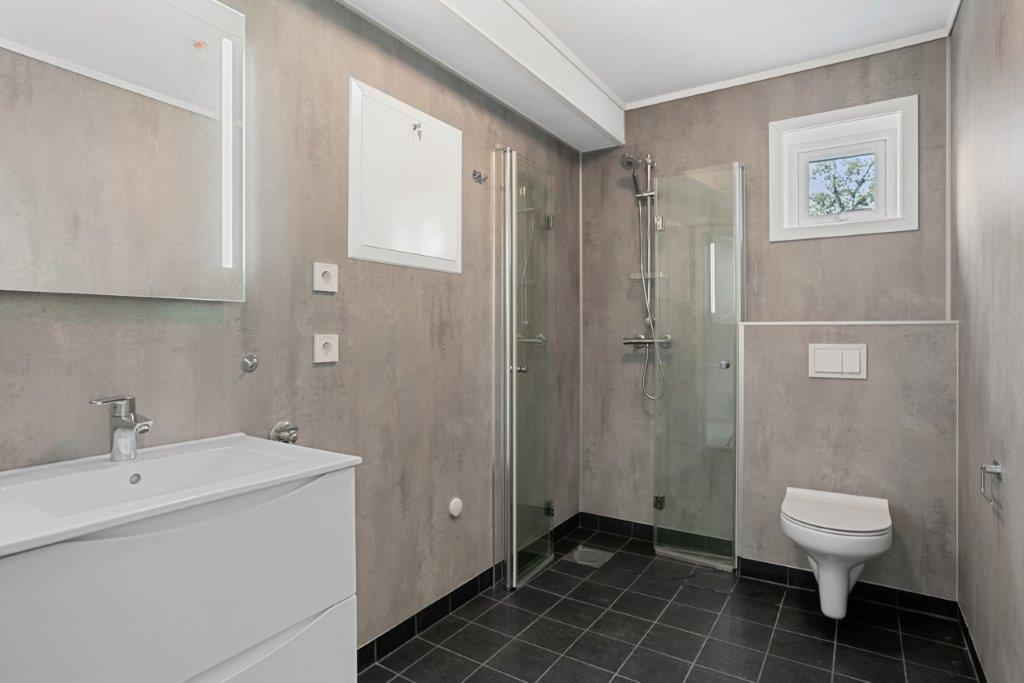 Stort baderom i nøytrale, lyse fargar og dusjhjørne. Foto.