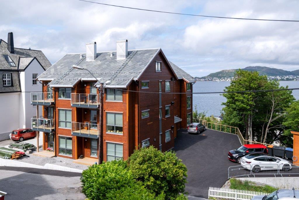 Oversiktsbilete av bustadene. Fasade langside i tre etasjar. Flott havutsikt. Uteareal med parkeringsplassar. Foto.
