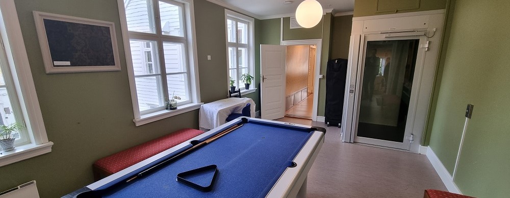 Grønt rom i fjerde etasje med blått biljardbord midt i rommet, tre hvitmalte vinduer ut mot bakgården, kuppellampe mist i rommet og dør til løfteplattform. Foto.