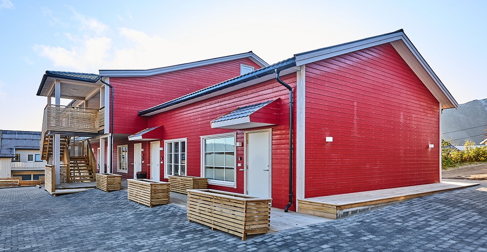 Bakside med inngangspartier, hvite dører og vinduskarmer, trehvite blomsterkasser ved hver dør, trapp opp til andre etasje. Foto.