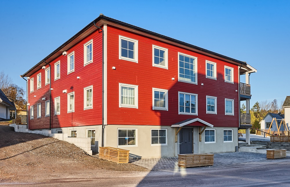 Fasade med tre etasjer, sett fra bakkeplan. Like store vinduer rundt hele, kjellerinngang midt i bygget. Foto. 