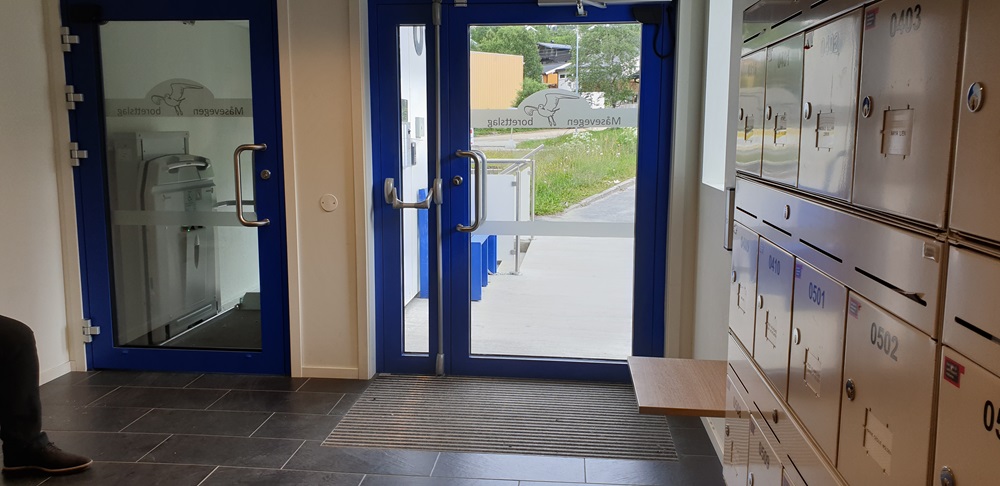 Inngangspartiet fra innsiden, tilgjegelige postkasser og løfteplattform fra bolig og til butikk i første etasje. Foto.