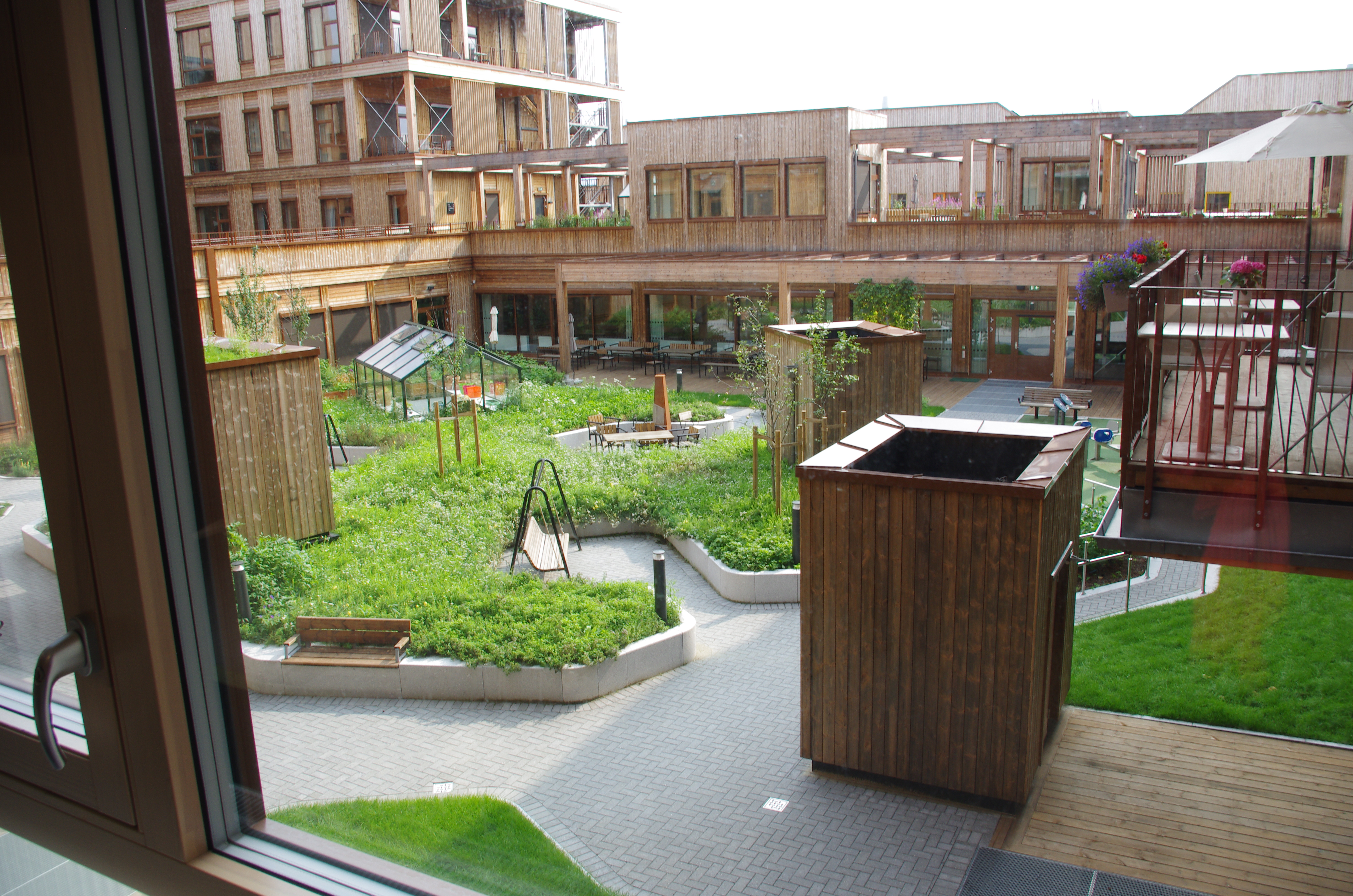 Indre hage med drivhus, planter  og benker. Foto.