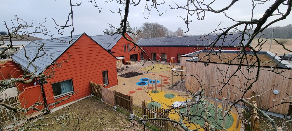 Utvendig oversikt over dei raude bygningane med leikeplass i midten. Foto. 