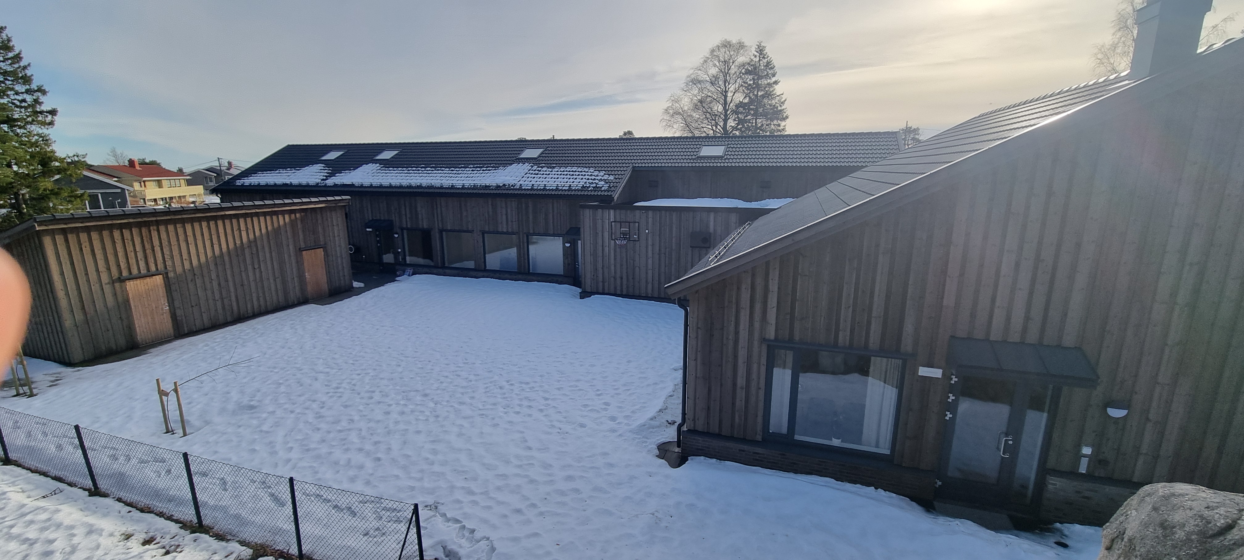 Bakgården formet som en U med en stor utebod. Snødekt bakke. To utganger fra svalgang og én fra fellesrom ved peisen. Foto. 