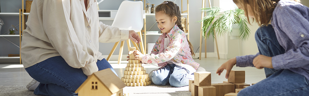 familie sitter på stuegulvet og bygger hus med byggeklosser