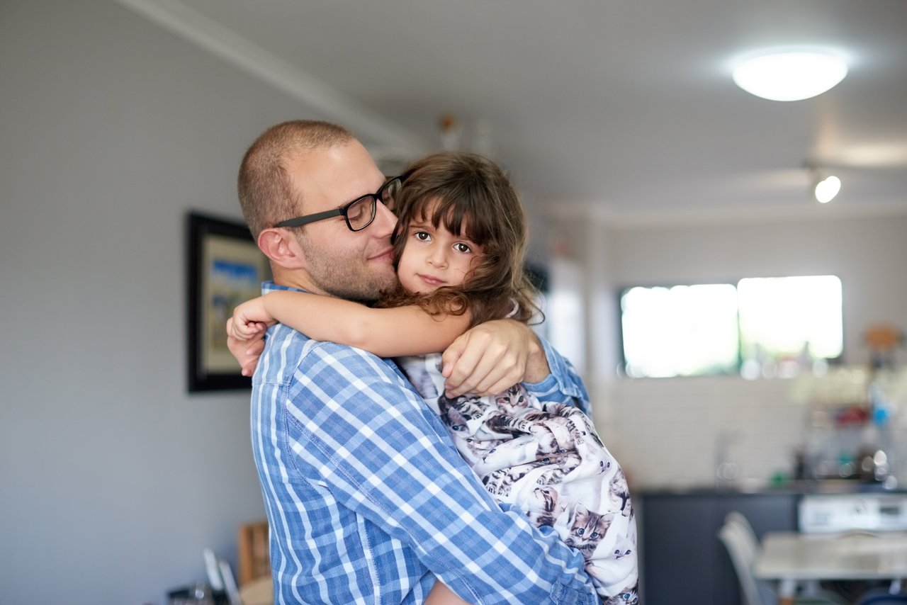 En far holder sin datter i armene i en leilighet. Foto.