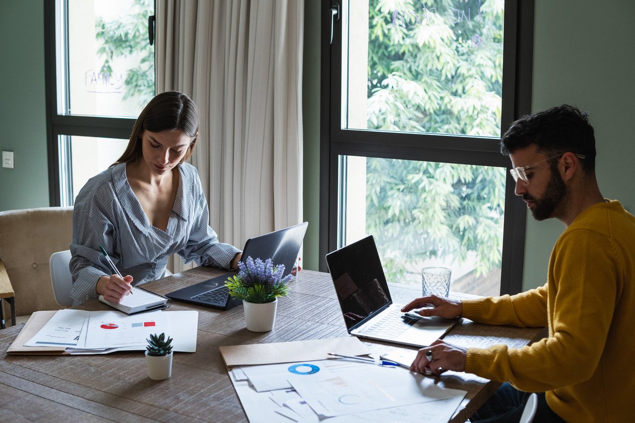 To studenter, en mann og en kvinne, sitter ved et bord med pc og bøker. Foto.